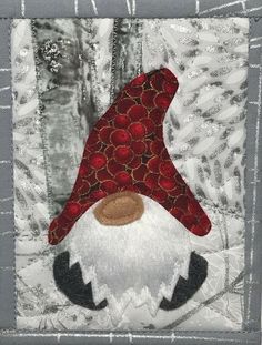 a gnome patchwork piece with red and white colors on it's face, sitting in front of a tree