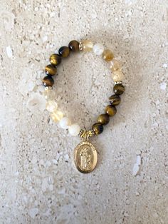 Saint Francis Bracelet featuring 8MM smooth golden tiger eye and gold rutilated quartz stones accented with gold spacers and Saint Francis of Assisi Medal.  Saint Francis is known to be the patron Saint for pets and animals.  Bracelet is beaded on stretch cord and measures 7 inches. GIFT BOXED Saint Francis Of Assisi, Catholic Bracelet, Golden Tiger, Saint Francis, Francis Of Assisi, St Francis, Patron Saints, Religious Gifts, Rutilated Quartz