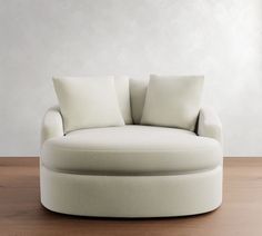 a white couch with pillows on top of it in front of a wall and wooden floor