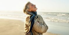 an older woman standing on the beach looking up at the sky with her eyes closed