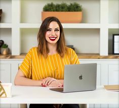 a woman sitting at a table with a laptop computer in front of her, smiling