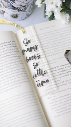 an open book with writing on it next to some flowers and reading utensils