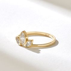 a yellow gold ring with two pear shaped diamonds on it's side, sitting on a white surface