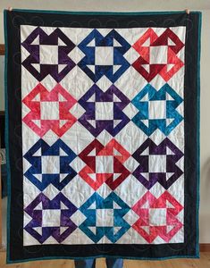 a person holding up a quilt made with different colored squares and arrows on it's back