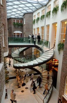 people are walking up and down the stairs in an indoor shopping mall with glass roof