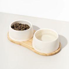 two white bowls with food in them on a wooden tray