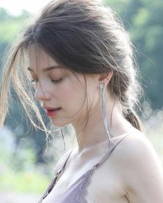 a woman with long hair wearing earrings and looking down at her cell phone while standing in the grass