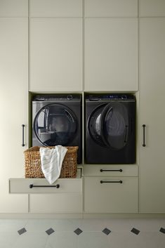 two washers and a dryer in a laundry room with white cabinets on the wall