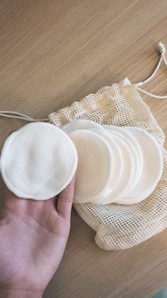 a hand is holding several pieces of cloth on a wooden table next to a string bag