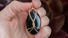 a person is holding a black stone in their left hand and gold wire wrapped around it