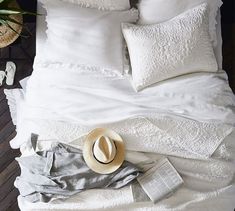 a white bed topped with pillows and blankets next to a hat on top of a wooden floor