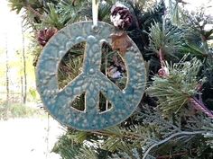 a peace sign ornament hanging from a tree with pine cones in the background