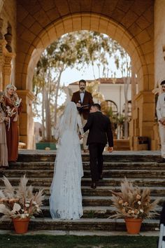 the bride and groom are walking down the stairs at their wedding ceremony in front of an archway