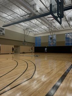 people playing basketball in an indoor gym with hard wood flooring and metal ceiling beams