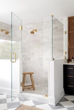 a bathroom with a checkered floor and white walls, glass shower doors, gold handles on the faucet