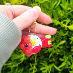 a hand holding a red and green toy in it's palm with grass behind it