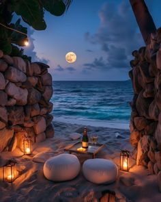 an outdoor seating area on the beach at night with lanterns lit up in front of it