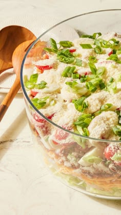 a salad in a glass bowl on a table with a wooden spoon next to it