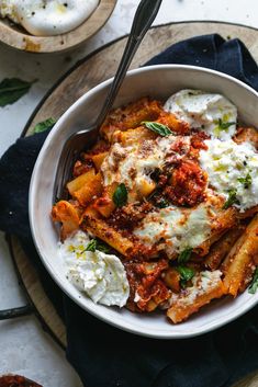 a white bowl filled with pasta and sauce on top of a wooden table next to other dishes