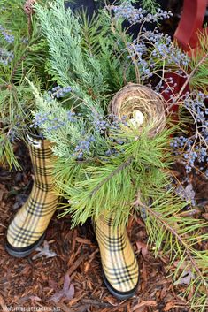 a pair of yellow rubber boots sitting on top of a pile of pine needles and blue flowers