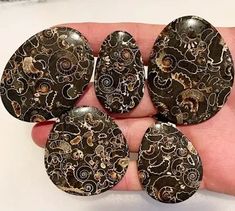 five pieces of black and gold glass with swirls on them, sitting in a person's hand