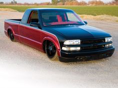 a red and black truck parked on the side of a road next to a field