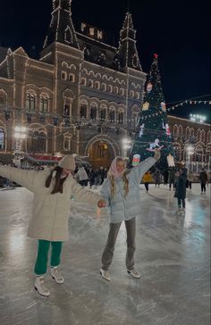 two girls skating on an ice rink in front of a large building with christmas lights