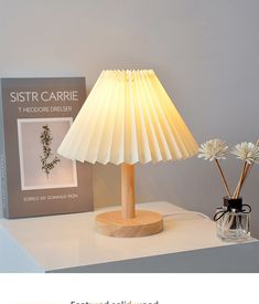 a lamp that is on top of a table next to a book and vase with flowers