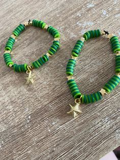 two green and gold beaded bracelets sitting on top of a wooden table