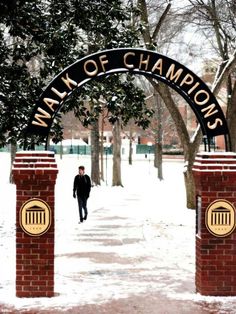 a man walking down a snow covered sidewalk next to a red brick arch with the words walk of champs on it