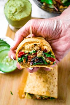 a hand holding a tortilla filled with meat and veggies next to a bowl of guacamole