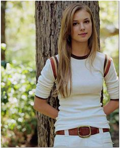 a woman standing in front of a tree with her hands on her hips and looking at the camera