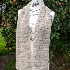 a white mannequin wearing a crocheted scarf in front of an apple tree