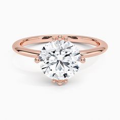 a rose gold engagement ring with a round cut diamond in the center, on a white background