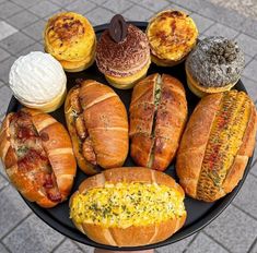 an assortment of breads and pastries on a black platter with a brick sidewalk in the background