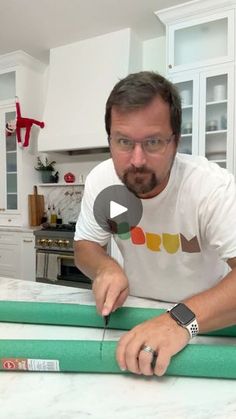 a man cutting green paper with scissors on a counter top in a white kitchen area