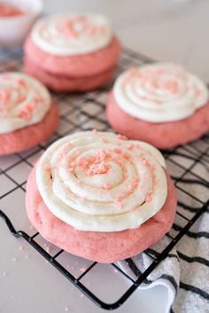 pink cookies with white frosting and sprinkles on a cooling rack