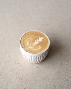 a cup of coffee with a leaf design on the top sits on a beige surface