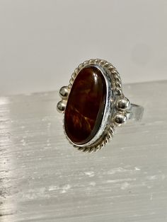 "Mexican Fire Agate set in Sterling Silver with a southwestern design work. The Fire Agate is a natural stone with a dark brown base color and bubbles of \"Fire\". This beautiful stone measures 19 mm by 10 mm. It is bezel set in Sterling Silver and has a rope design setting. The ring is measures 21mm long x 17mm wide. The band tapers to 4 mm Size- 7 Marked- none (tested and confirmed sterling Silver) Weight-4.58g" Artisan Brown Gemstone Rings, Brown Oval Agate Rings, Oval Brown Agate Rings, Brown Oval Cabochon Rings, Brown Oval Rings With Natural Stones, Oval Brown Rings With Natural Stones, Oval Brown Ring With Natural Stones, Unique Brown Oval Rings, Fire Agate Ring