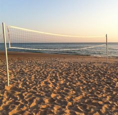 a volleyball net on the beach with waves in the water behind it and sand covering the ground