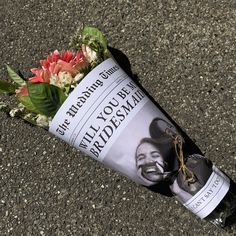 a bouquet of flowers is placed on the ground next to a newspaper roll that has been rolled up