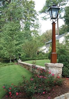 a lamp post sitting in the middle of a flower bed next to a sidewalk and trees