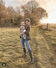 a woman holding a small dog in her arms while standing on top of a grass covered field