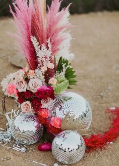 an arrangement of flowers and disco balls on the ground in front of some red feathers