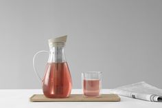 a pitcher and glass are sitting on a tray next to each other, with a newspaper in the background