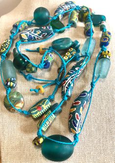 A beautiful combination of Ghana Krobo beads are hand-knotted to create this long necklace.  It is a one-of-a-kind piece. -  Handmade, one-of-a-kind. -  Lovely combination of teal and yellow Ghana Krobo beads, sandcast, fused glass, ceramic, and recycled glass beads. -  The hand-knotting and spacing allows for each bead to be individually showcased. -  Necklace measures 36" in length and is not adjustable. -  Beads are strung on teal hemp cord. -  Brass "hand made" charm tag. -  Comes with jewel Hippie Style Green Beaded Necklace For Festivals, Bohemian Multi-strand Hand Wrapped Beads, Artisan Adjustable Beaded Necklaces For Beach, Unique Recycled Glass Necklaces For Beach, Unique Recycled Glass Beach Necklace, Hippie Style Green Beaded Necklaces With Round Beads, Bohemian Turquoise Fair Trade Jewelry, Bohemian Turquoise Jewelry Fair Trade, Bohemian Turquoise Jewelry, Fair Trade