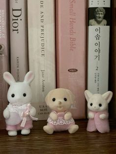 three small stuffed animals sitting next to each other on a book shelf with books behind them