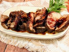 meat with sauce and parsley sitting on a white plate next to a wooden table