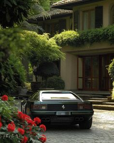 a black car parked in front of a house with red flowers on the side walk