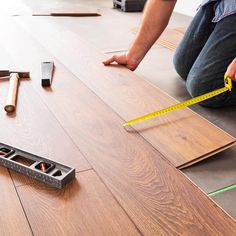 a man measuring the width of a hardwood floor with tape measures on top of it